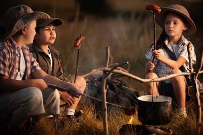 3 enfants font griller leurs saucisses à l'occasion d'un feu de camp en colo