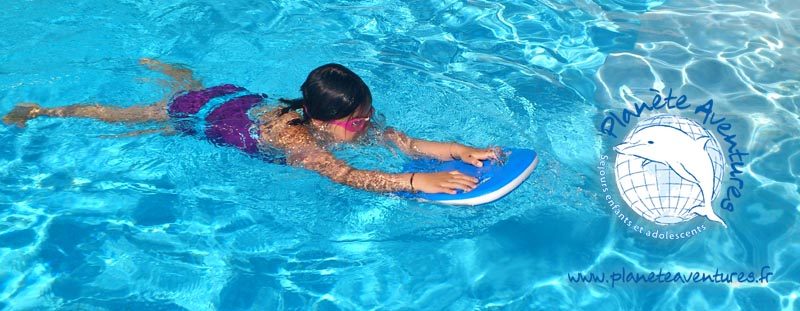 Un petit garçon apprend à nager en piscine avec une planche